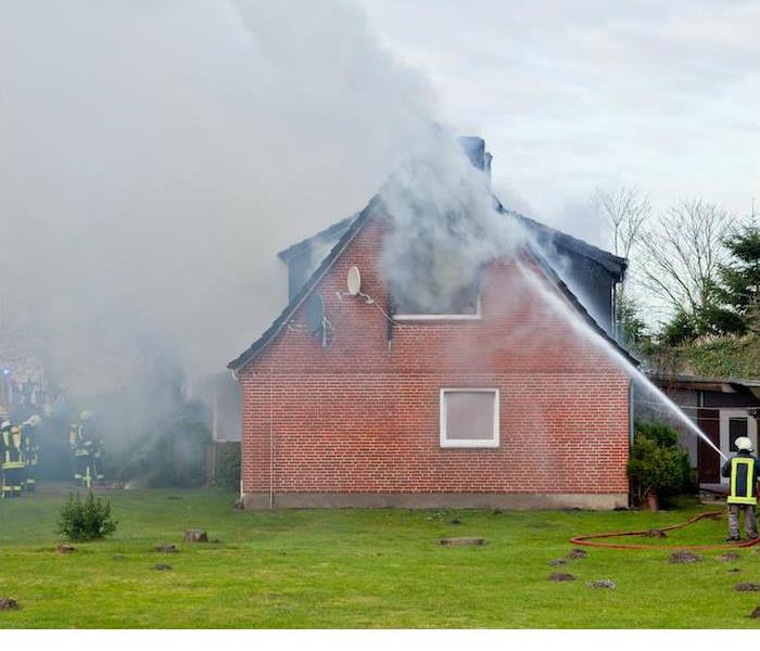 Firefighters extinguishing a fire at a large brick house
